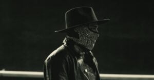 Artist wearing a hat and face mask in a dark setting.