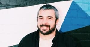 Carlos Grassot smiling in front of a colorful mural wall.