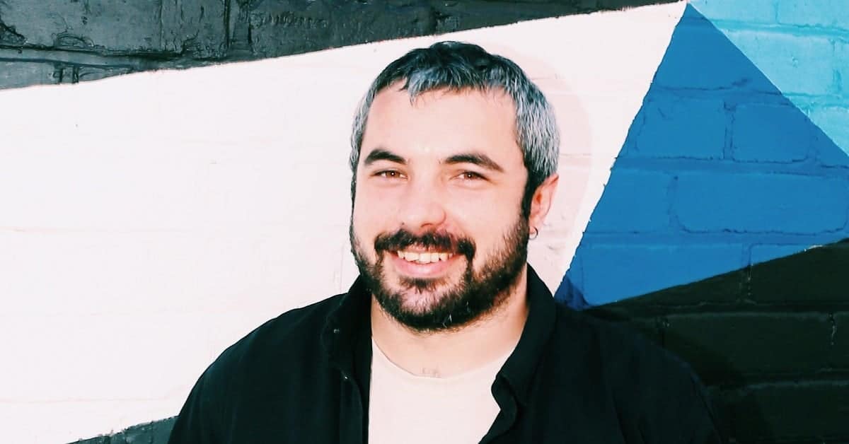 Carlos Grassot smiling in front of a colorful mural wall.