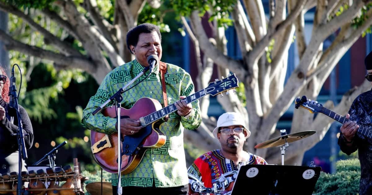 Musician playing guitar and singing outdoors during a live performance.