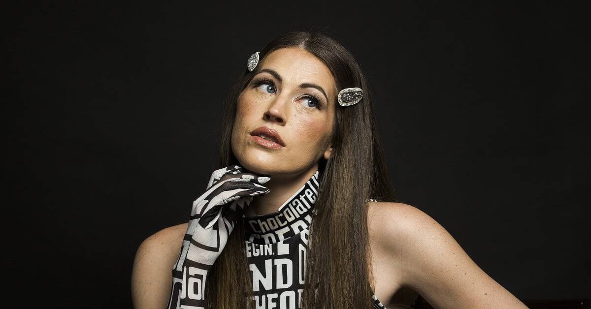 Samantha Davis with hair rollers and a thoughtful expression against a black background.