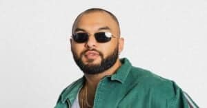 Hip-hop artist with sunglasses and beard in a green jacket.