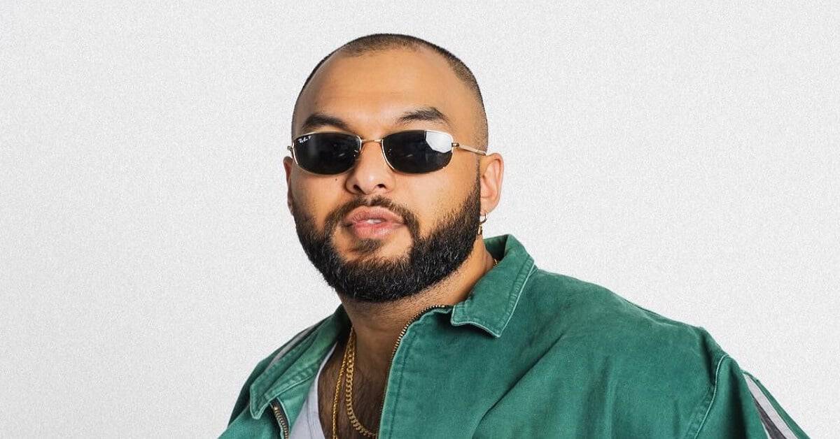 Hip-hop artist with sunglasses and beard in a green jacket.