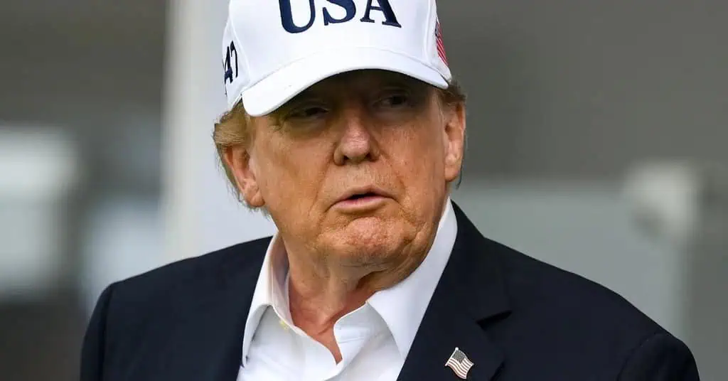 President Trump wearing a white 'USA' cap and dark suit.