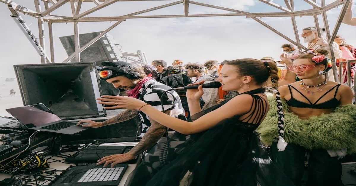 DJ mixing music at outdoor festival with crowd and sky in background.