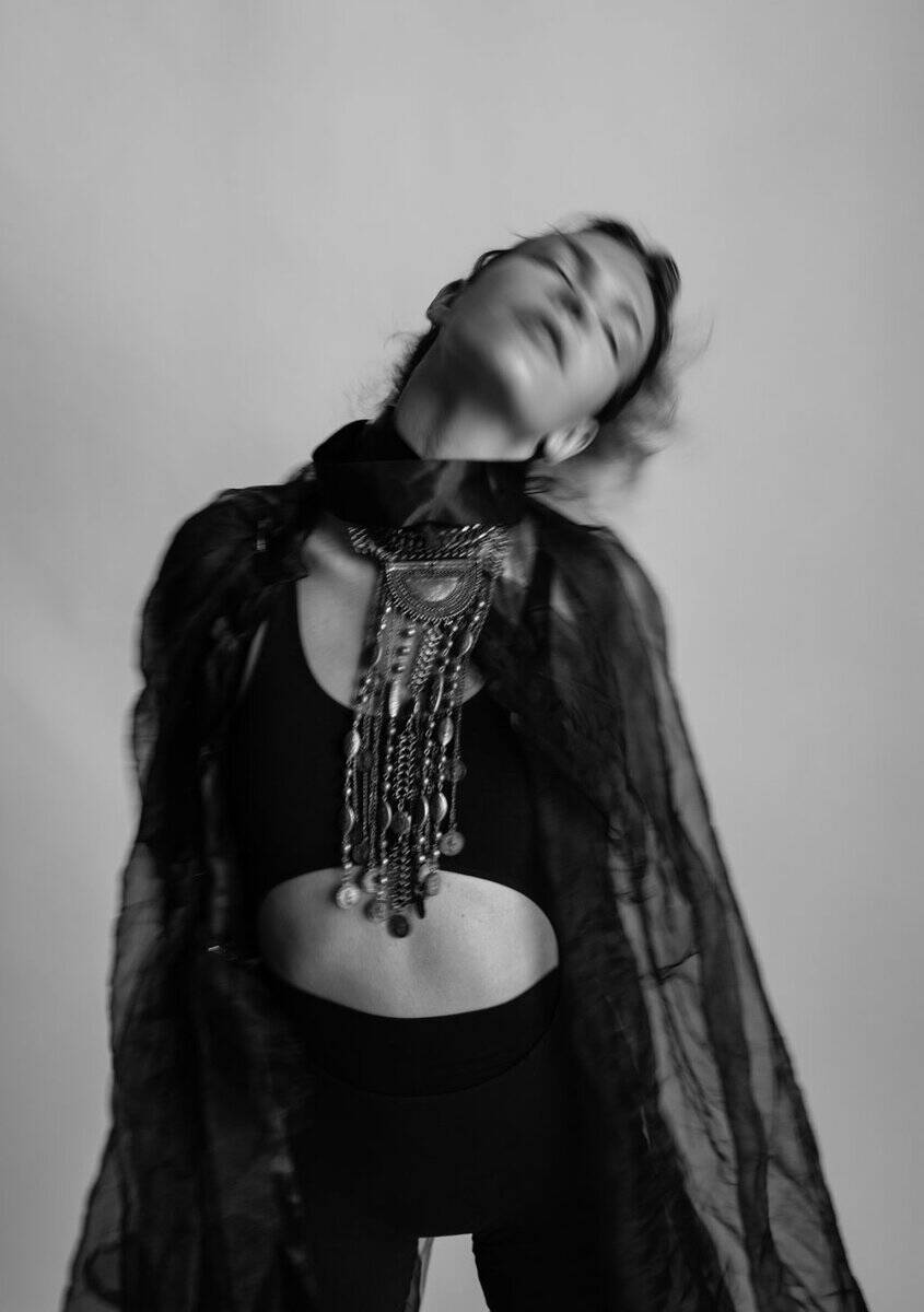 Black and white photo of a woman with her head tilted back, eyes closed, wearing layered jewelry.